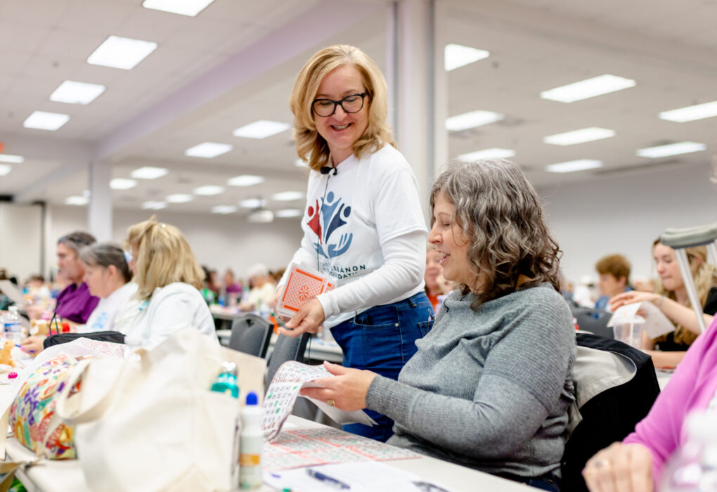 Woman with white shirt talking to woman in grey shirt in a crowded room