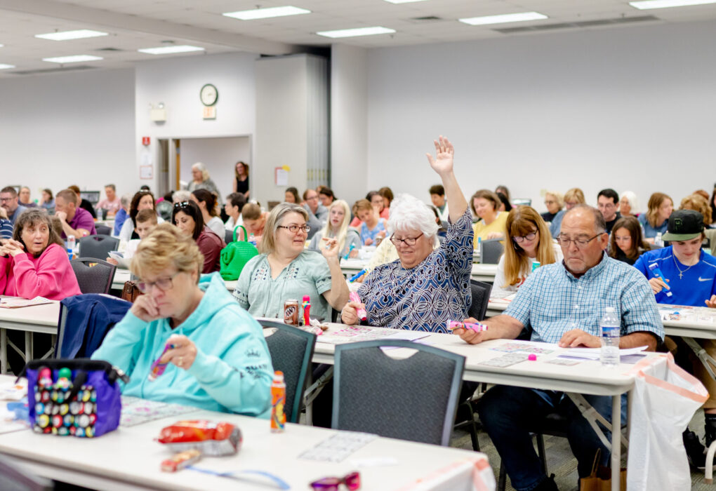 Woman with white hair raising her hand in a crowded room